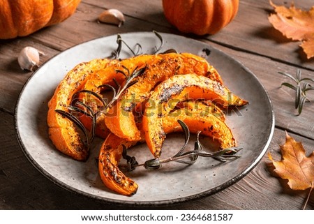Roasted pumpkin slices with garlic and herbs close up. Oven baked pumpkin, seasonal autumn side dish or vegan meal.