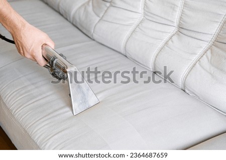 Professionally chemical cleaning. Cleaning concept. Man cleans sofa in the room, close up. Virus prevention sanitizing inside. The sofa is light gray or white.  Royalty-Free Stock Photo #2364687659