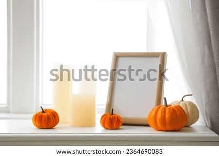 Blank frame with pumpkins and candles on mantelpiece in room, closeup