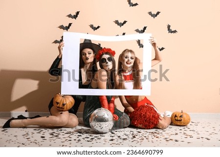 Female friends dressed for Halloween with frame near beige wall
