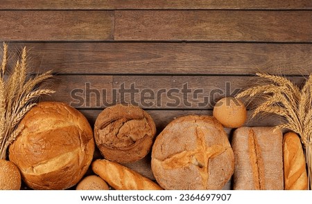 Freshly baked whole grain homemade bread, assorted varieties of round sourdough bread with crispy crust and ears of rye and wheat on a wooden background with space for text, modern baking concept,