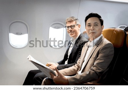 Senior businessman holding newspaper, sitting in comfortable seat inside airplane, male passenger talking in aircraft cabin during business trip, businesspeople traveling with airline transportation. Royalty-Free Stock Photo #2364706759