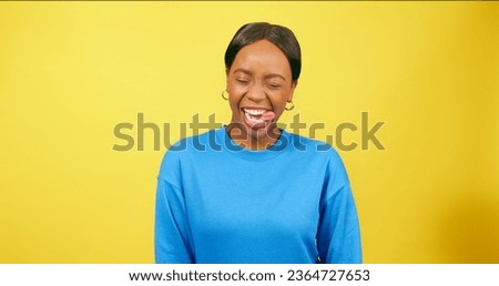 Cute young woman pulls funny face, sticking tongue out, yellow studio background