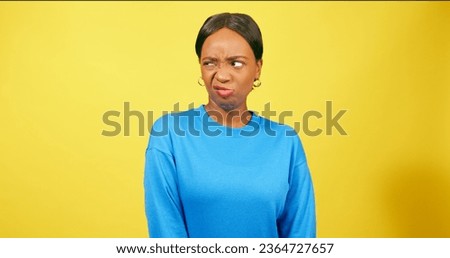 Cute young woman pulls funny face, grimace, yellow studio background