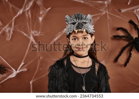 cute girl in black outfit with wolf mask on brown background, close up, Halloween concept