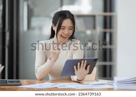 Excited happy young Asian woman winner and celebrating success at desk in office. Royalty-Free Stock Photo #2364739163
