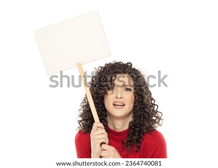 Young curly unhappy woman holding blank sign on white studio background.