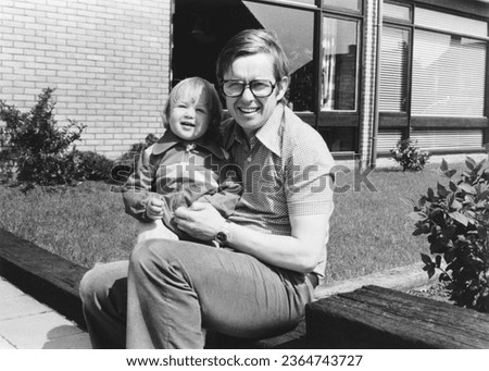 1978 vintage, seventies, retro roll film monochrome portrait of father and daughter sitting in front of a house in the summer sun.	