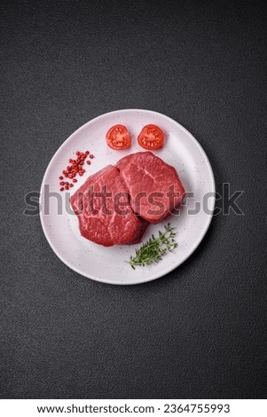 Raw fillet steak mignon beef with salt, spices and herbs on a dark concrete background