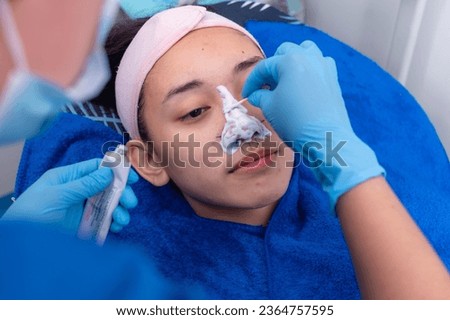 Applying topical anesthesia via a cotton swab to the nose to numb the skin. Preoperative procedure for an open rhinoplasty procedure.
