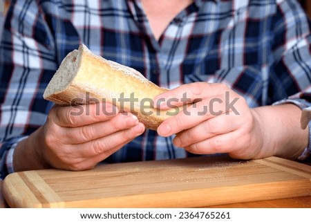 Hands of an elderly woman holding sliced white wheat bread baguette in the kitchen at a brown table, no face, close-up