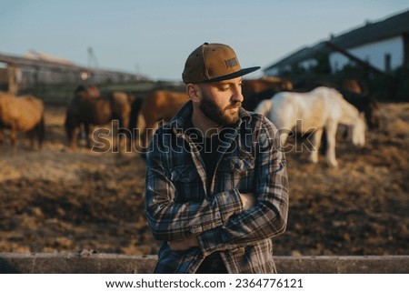 Portrait of a young farm worker, on the background of a fence with horses. A young farmer takes care of horses in the stables.