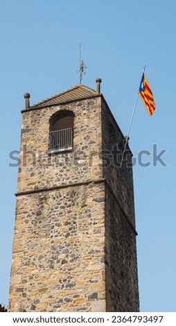 Catalan flag waving in the blue sky on an ancient medieval tower. Red and yellow striped flag on historic stone building.