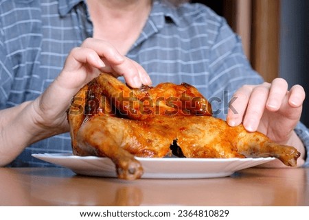 The hands of an elderly woman operate a grilled chicken and display it in the kitchen at a brown table, without a face, close-up