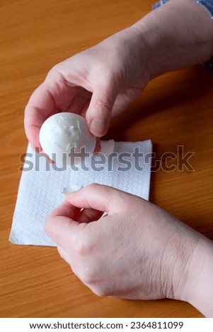 Hands of an elderly woman showing a white boiled egg and peeling it in the kitchen at a brown table, no face, close-up