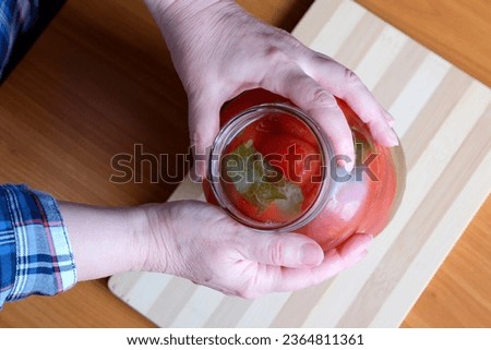 The hands of an elderly woman take out delicious homemade pickled tomatoes from a jar in the kitchen at a brown table, without a face, close-up