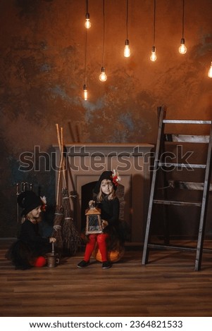 Girls in witch costumes are sitting near the fireplace on pumpkins, one is holding a lantern, the other is making a potion. Halloween. Vertical frame.