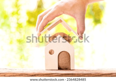 Loan for real estate concept, Man hand holding the roof house and  money bag and  the  home model put on the wood in the public park.