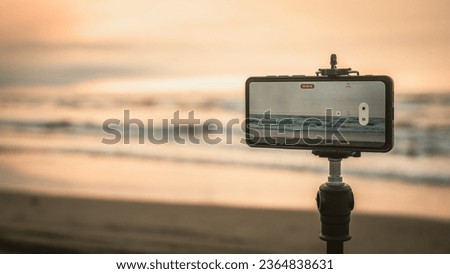 Smartphone on a tripod filming the sea at sunset in golden time.