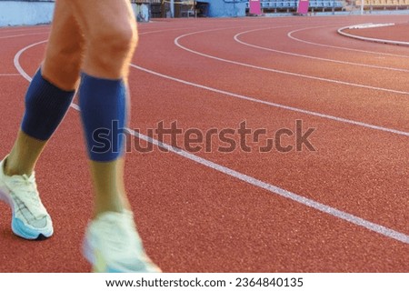 Half-blurred legs of a runner in motion on a running track around the stadium. Object on the left with space for text. Royalty-Free Stock Photo #2364840135