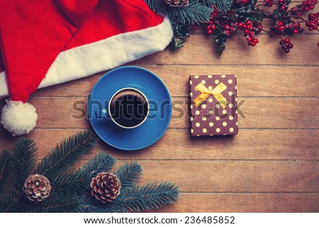 Cup of coffee and gift box with pine and hat on wooden table.