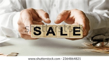 SALE inscription on the texture of wooden cubes. A business man holds a cube in his hand. An inscription on a financial, business or economic theme.