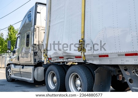 Beige industrial grade big rig semi truck tractor with broken dry van semi trailer fastened by sling standing on the city street waiting for possible repair or replacement of deformed trailer parts Royalty-Free Stock Photo #2364880577