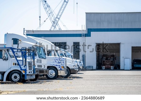 Different makes and models of the big rig semi trucks standing in row on industrial parking lot waiting for maintenance and repair in mechanical workshop boxes Royalty-Free Stock Photo #2364880689