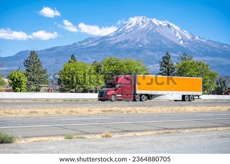 Industrial long hauler carrier burgundy big rig semi truck tractor transporting commercial cargo in dry van semi trailer running on the highway road with snow mountain on the background in California
