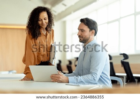 Portrait of positive businesspeople African American woman and hispanic man, using laptop, sitting at workplace in modern office. Concept of successful business Royalty-Free Stock Photo #2364886355