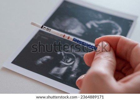 Woman holding a positive pregnancy test on the background of a photo with an ultrasound. 