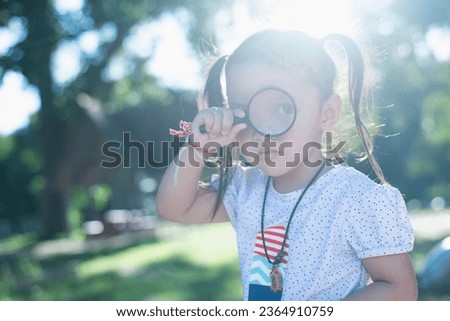 Asian little girl is using magnifying glass to play in the park