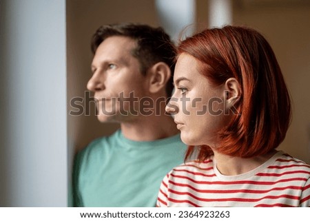 Unsmiling man and woman look out window. Guy and girl, young romantic married couple seriously watching what happening outdoor frustrated disappointed by cloudy cold weather outside. Close up portrait Royalty-Free Stock Photo #2364923263