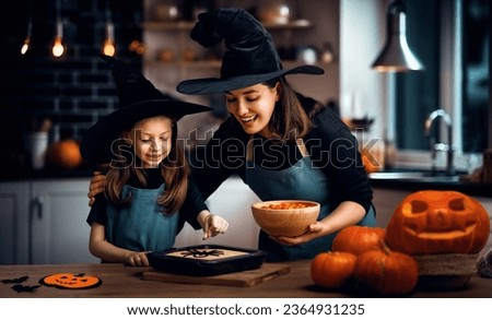 Mother and her daughter having fun at home. Happy Family preparing for Halloween. Mum and child cooking festive fare in the kitchen.