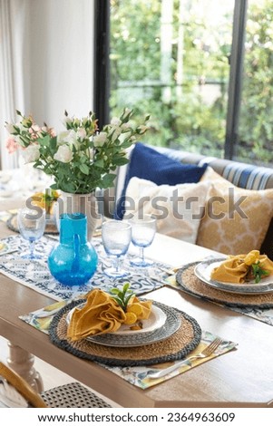 Plate setting with yellow handkerchief on wood table with artificial flowers on the dining table. 