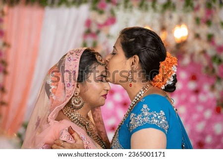 happy loving mother kissing daughters forehead by hugging her bridal daughter during wedding on stage - concept of Emotional Moment, parental blessings and traditional culture Royalty-Free Stock Photo #2365001171
