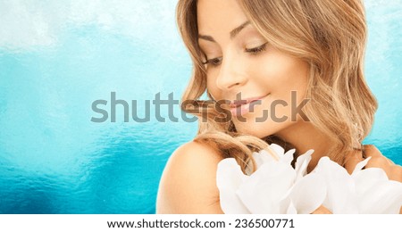 beauty, people and health concept - beautiful young woman with flowers and bare shoulders over ripple blue water background