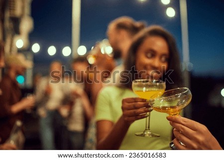 Focus on cocktail glasses clinking. Friends meeting at party on rooftop, having fun, enjoying good evening. Concept of party, leisure time, fun and joy, weekends, celebration, youth culture