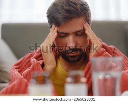 autumn and winter season of sneezes. Young Caucasian man with flu feels cold in living room at home, having fever and headache and touching his forehead to check his temperature. Royalty-Free Stock Photo #2365023331