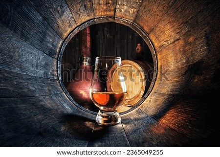 A glass of whiskey in old oak barrel. Copper alambic on background. Traditional alcohol distillery concept Royalty-Free Stock Photo #2365049255