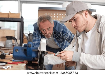 mature carpenter teaches student how to fix circular saw Royalty-Free Stock Photo #2365065863