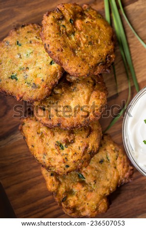 Delicious green zucchini pancakes stacked together and shot on a wood cutting board.  Green onions and a bowl of sour cream are pictured as well. 