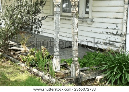 BROKEN DAMAGED DECKING ON AN OLD HISTORIC HOME Need a handyman or gardener?  Front porch with peeling flaking painted timber walls, worn, ruined floor boards with holes and overgrown weeds and plants.