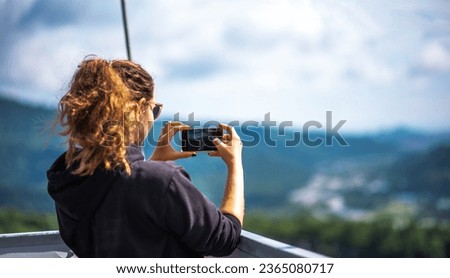 Young tourist woman using smart phone in the mountains, taking pictures. Girl makes a photo on the hiking on a summer sunny day. Girl using cell phone photography app.