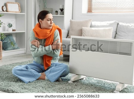 Young woman warming hands near radiator at home Royalty-Free Stock Photo #2365088633