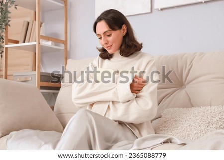 Young woman in warm sweater with book sitting on sofa at home