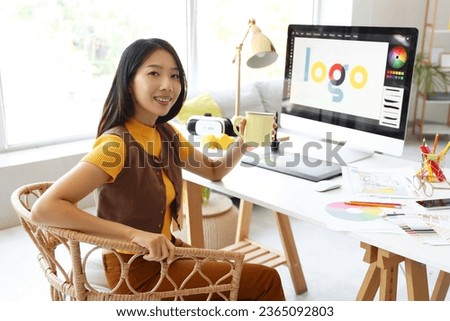 Asian interior designer with cup of tea sitting at table in office