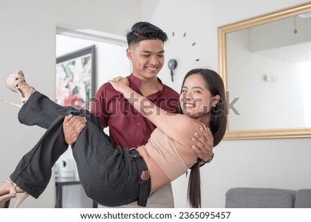 Newlyweds moving in at their condo apartment. A handsome man carrying his petite wife in his arms. Romantic and cheerful newlyweds.