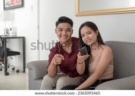 A young asian lady with her hubby hanging the channel or movie with a remote. A couple watching tv at the living room of their condo unit. Looking directly at the camera. Royalty-Free Stock Photo #2365095465