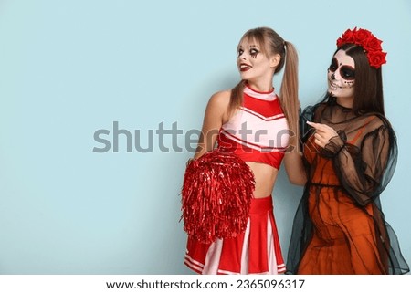 Female friends dressed for Halloween pointing at something on blue background